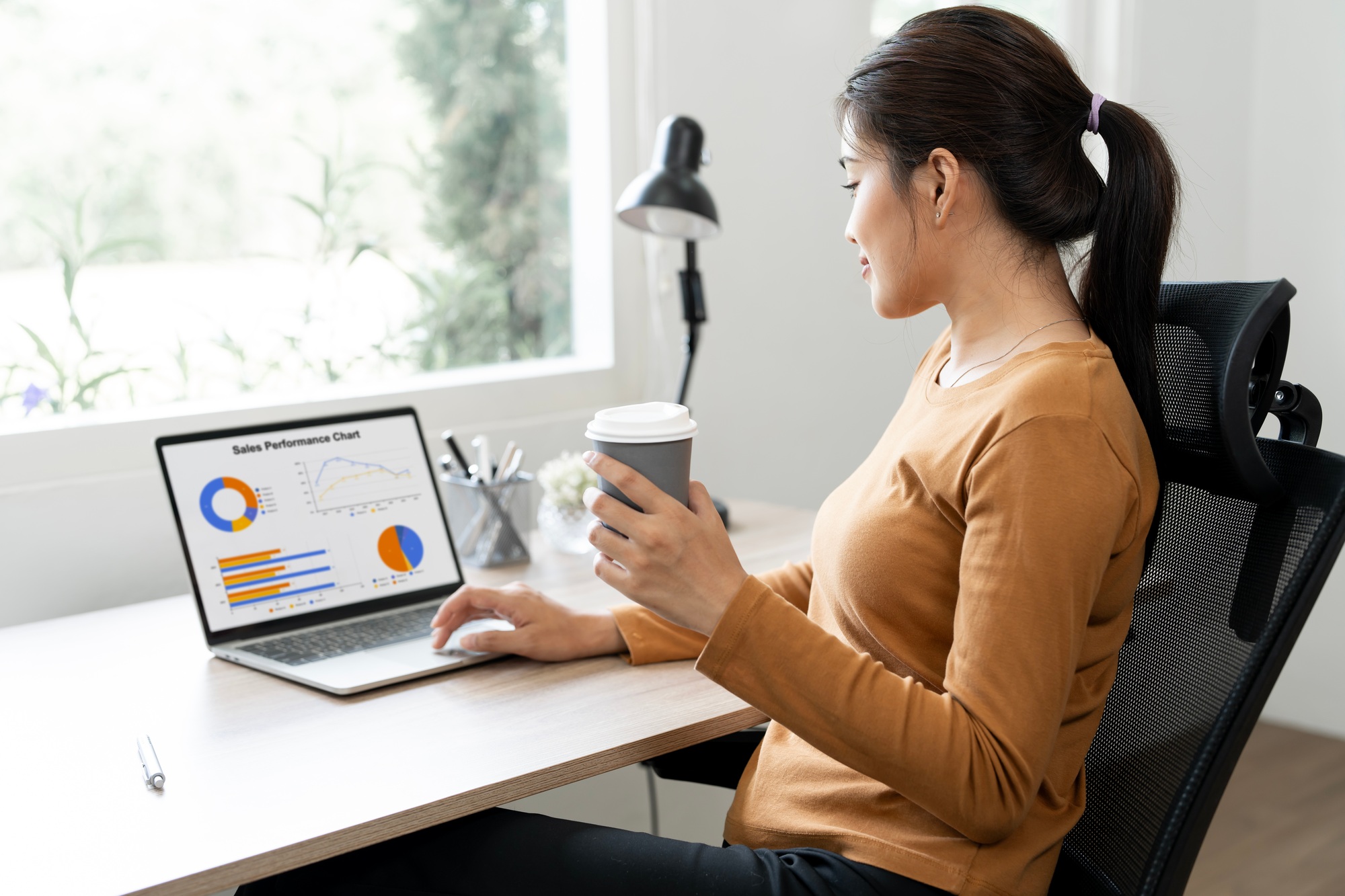 Woman analyzing financial data graphs, charts on laptop display at a modern home workspace.