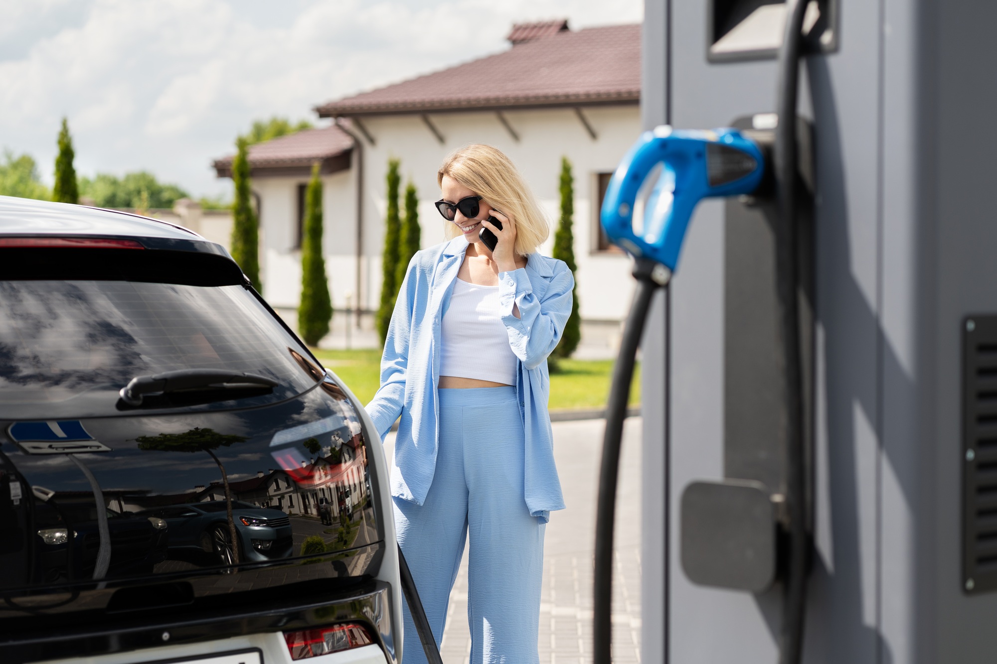 Woman Charging Electric Car While Talking on Phone at Charging Station
