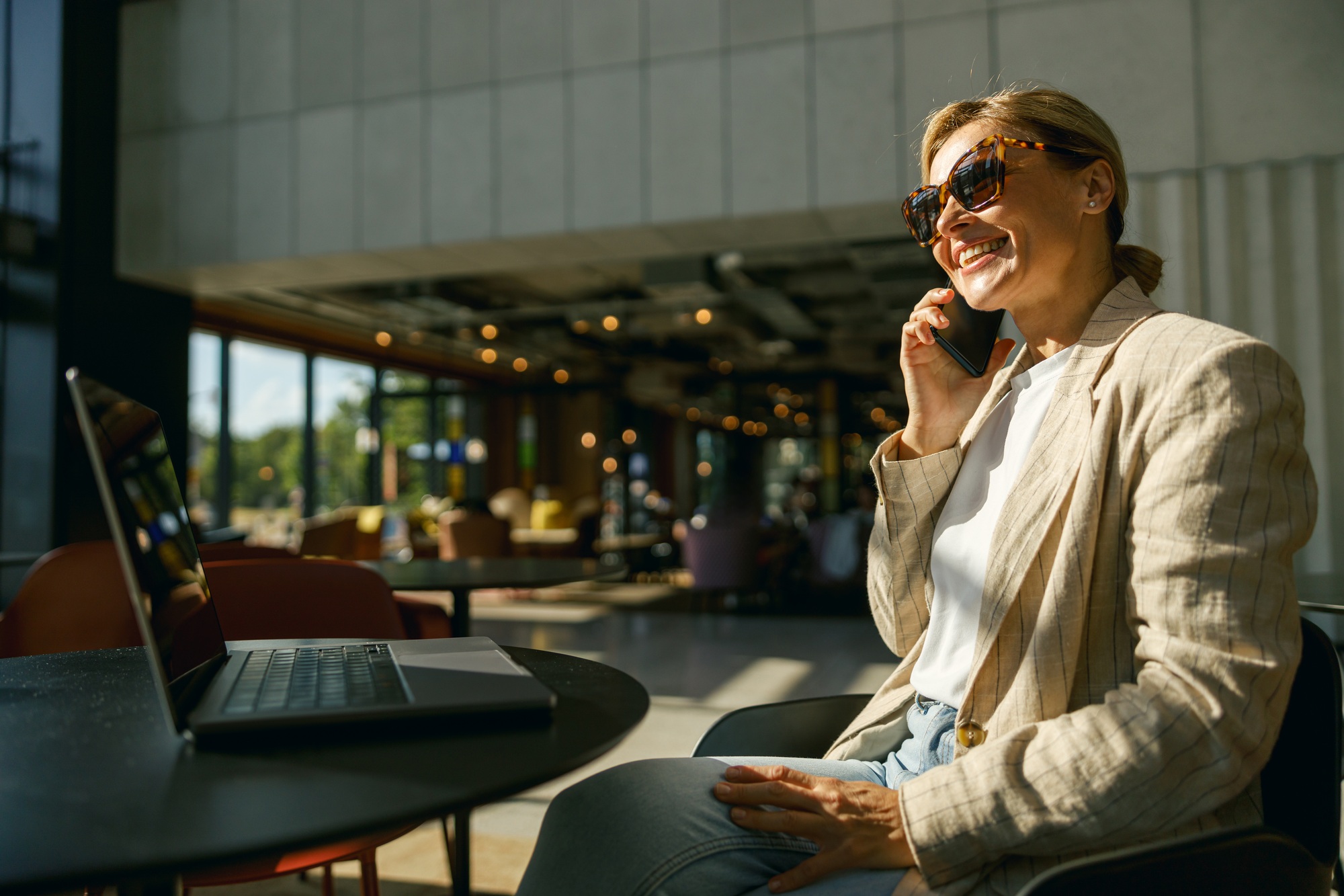 Woman freelancer talking on phone with client while working on laptop in modern coworking