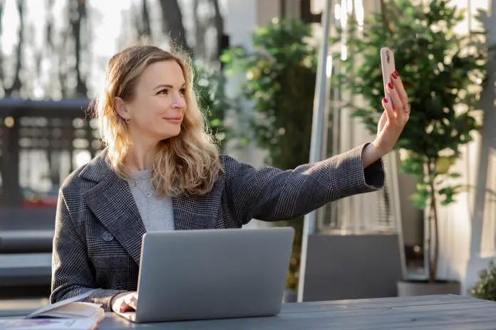 woman working laptop in park and taking video on phone online meeting