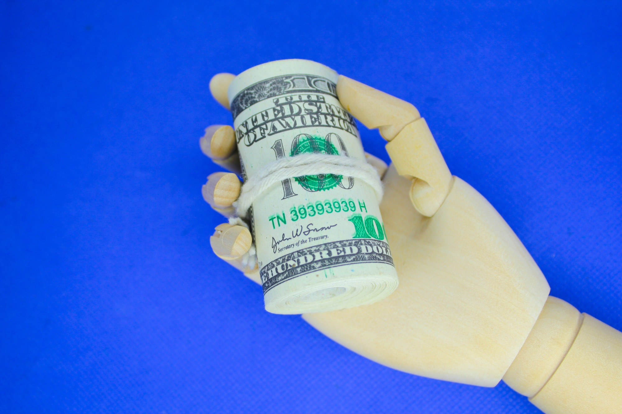 wooden hand holding a roll of paper money. the concept of making money