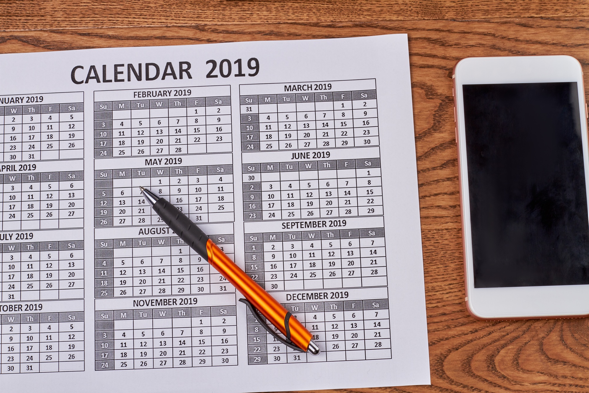 Year calendar with smartphone and pen on wooden desk.