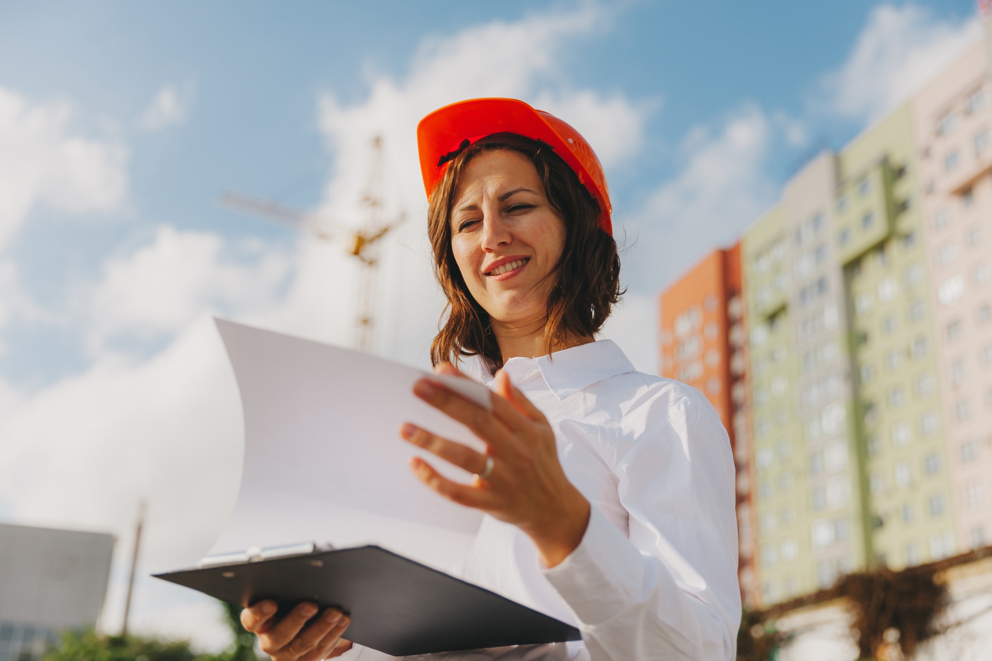 Young beautiful woman architect in white shirt and hard hat holding a flip board.