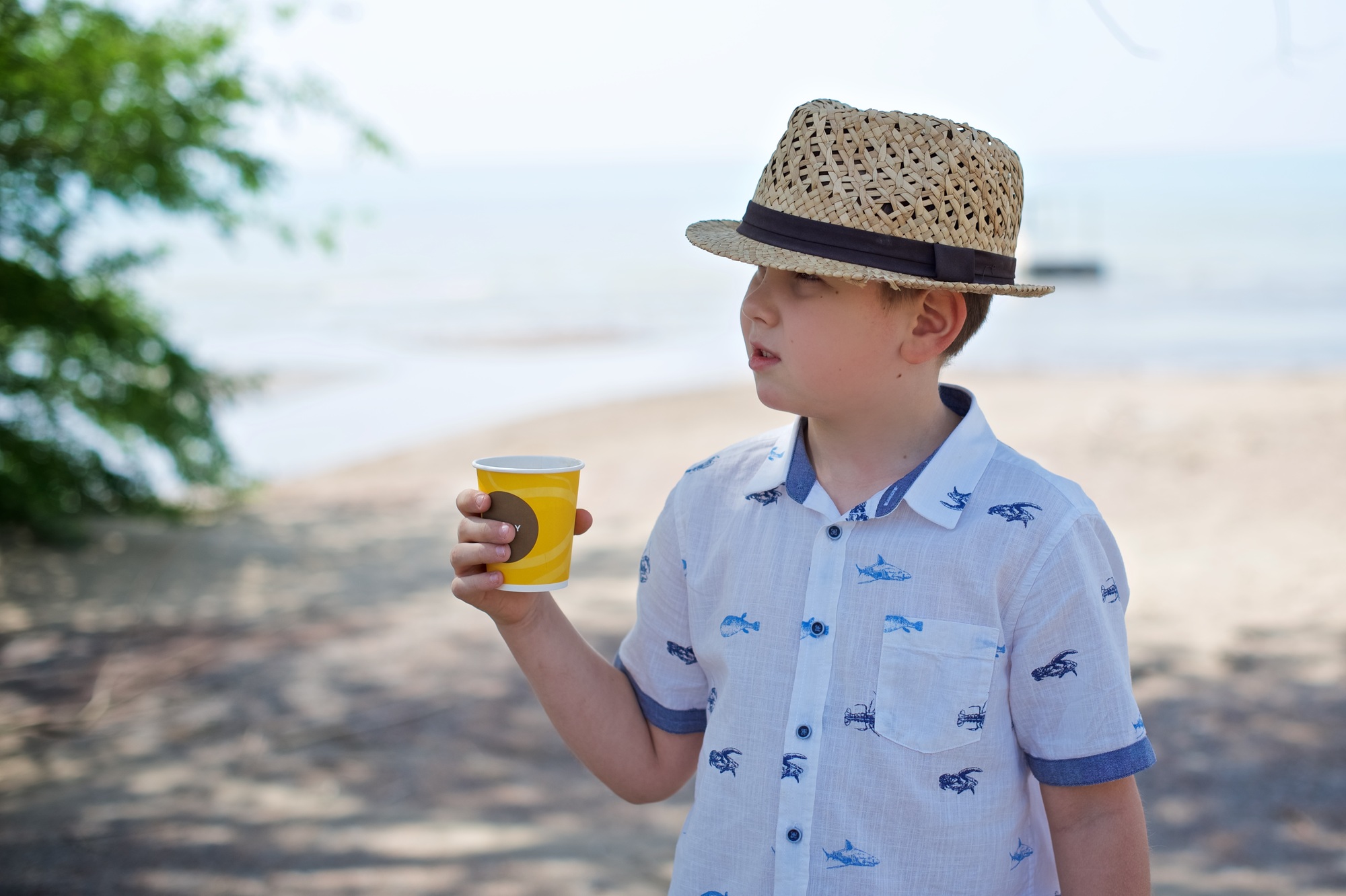 Young boy stands at the sand beach and drinking cold lemonade
