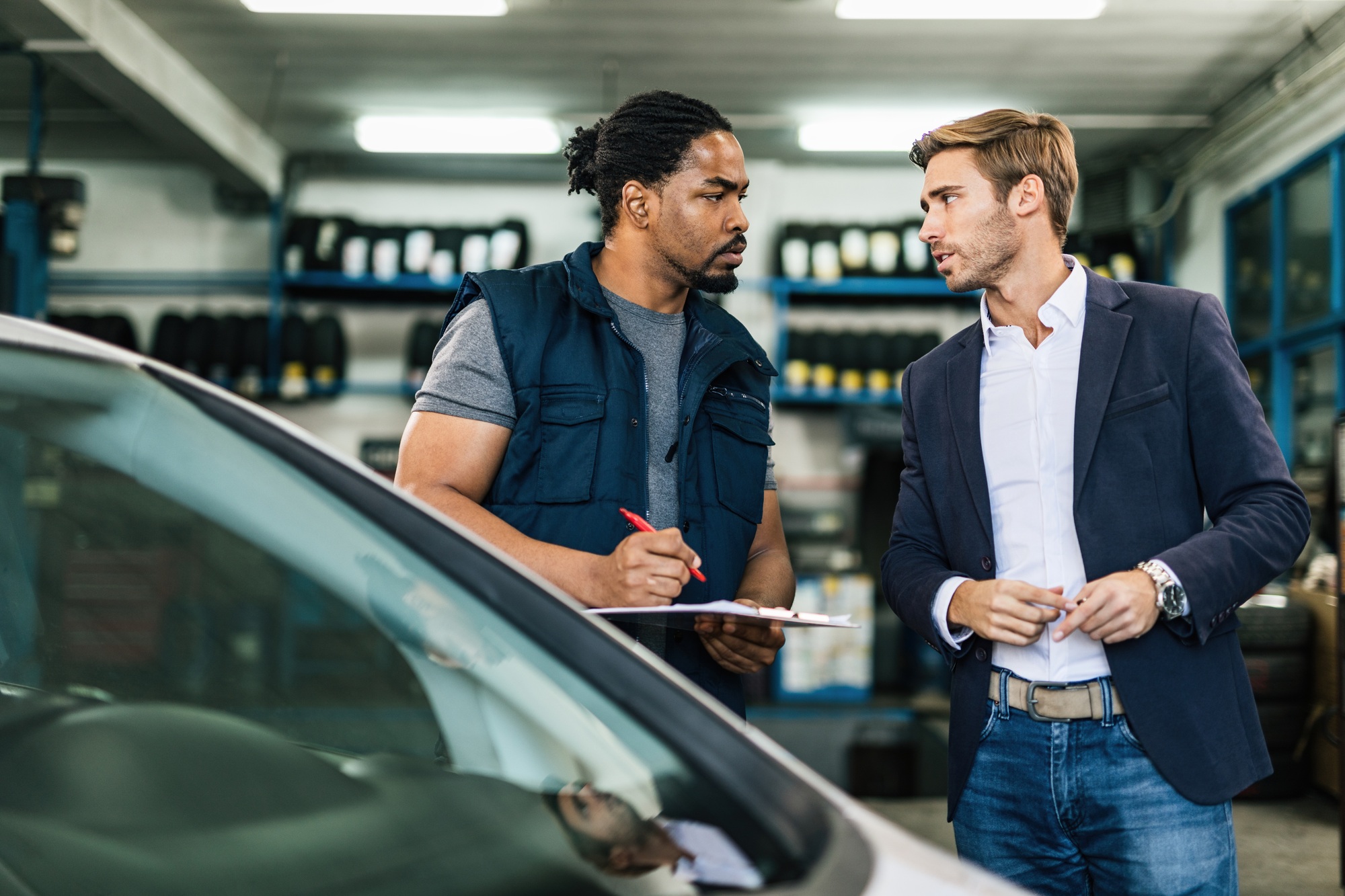 Young businessman communicating with African American auto mechanic in repair shop.