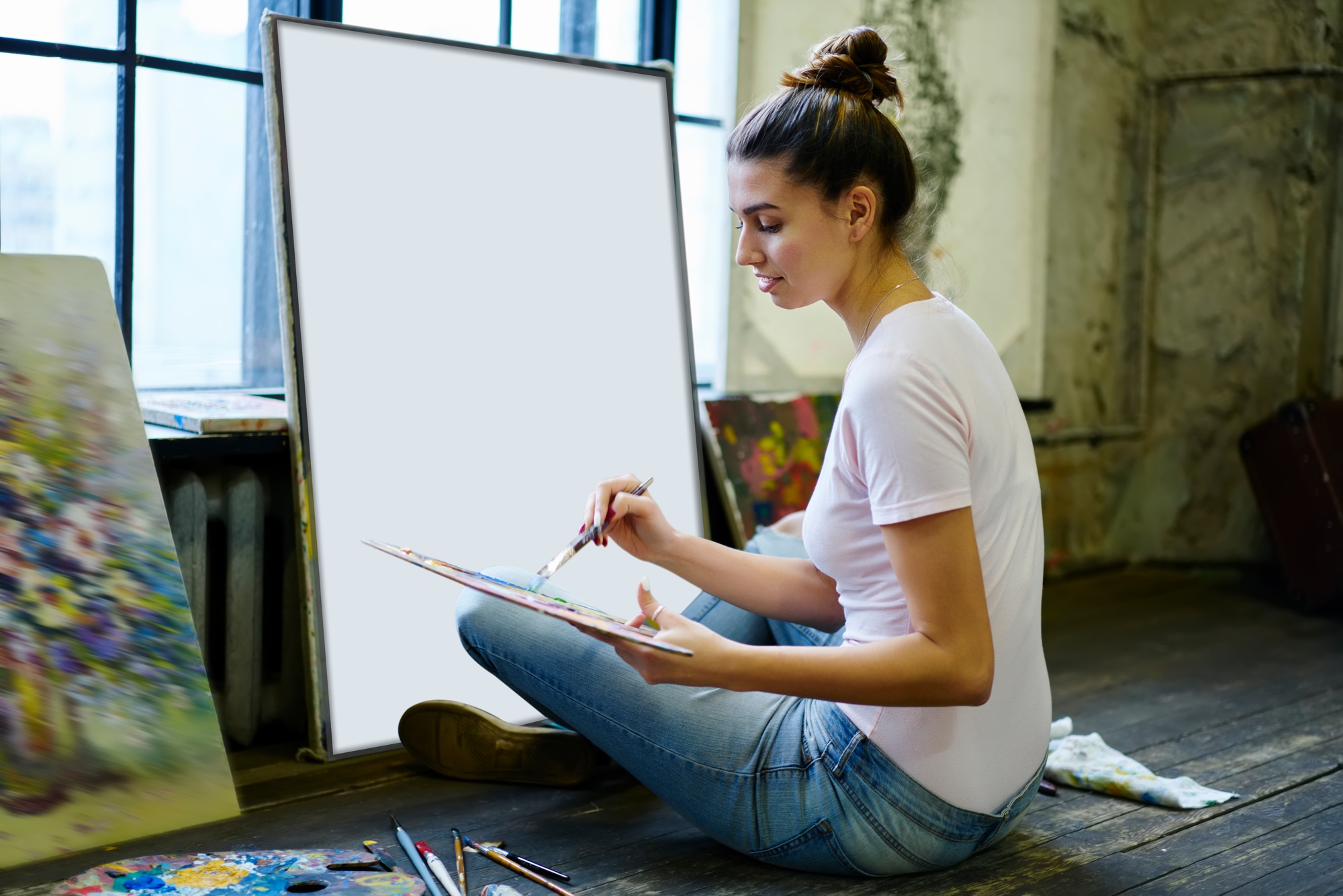 Young Caucasian amateur with pallet mixing acrylic colors sitting near canvas with sketch