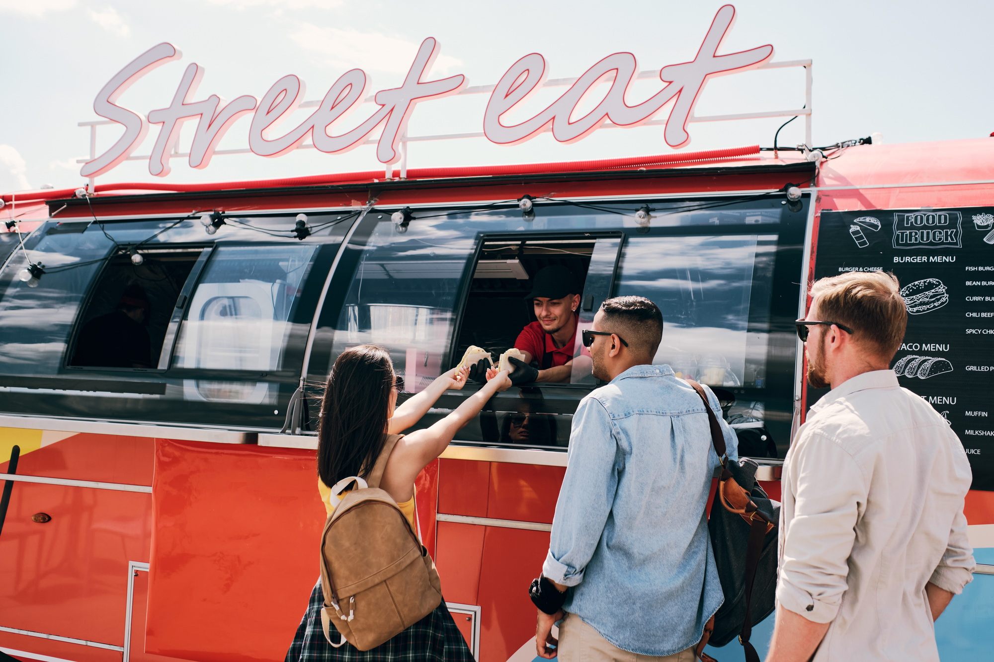 Young female buyer taking two hotdogs in food truck