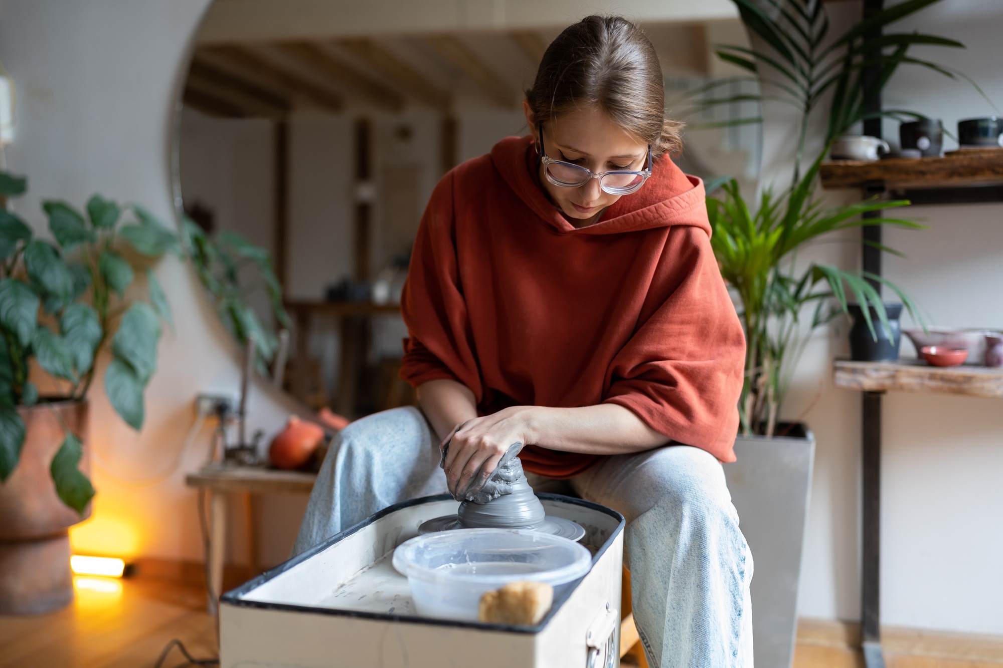 Young focused woman local ceramic artist working with clay on wheel in cozy ceramics studio