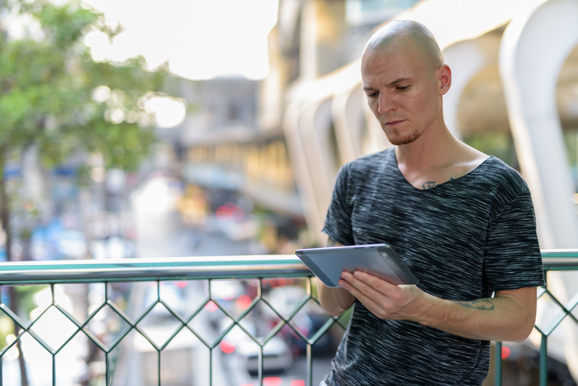 Young handsome bald man using digital tablet on the foot bridge