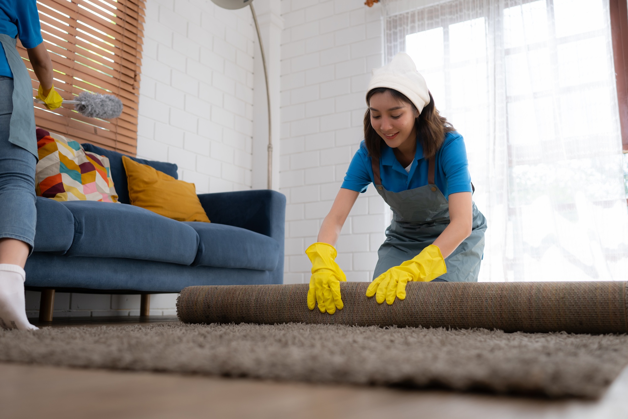 Young women cleaning maid in uniform and rubber gloves are cleaning the room, fold up carpet