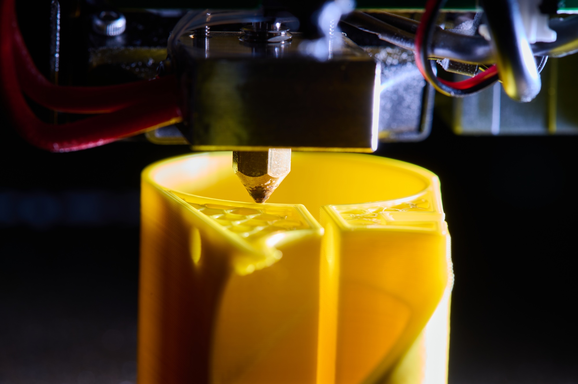 3D printer printing a part made of yellow plastic, close-up view