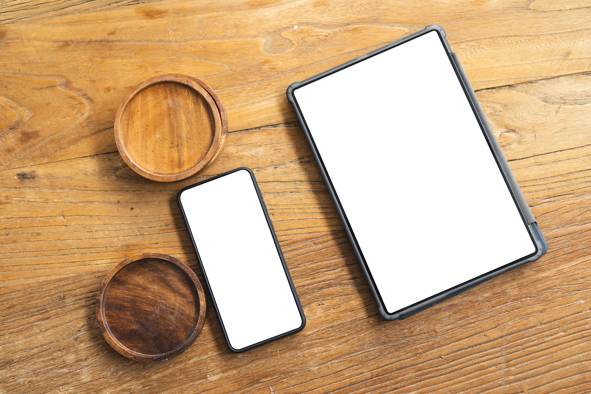 A smartphone and a tablet with blank screens lie next to two small wooden bowls on a textured table,