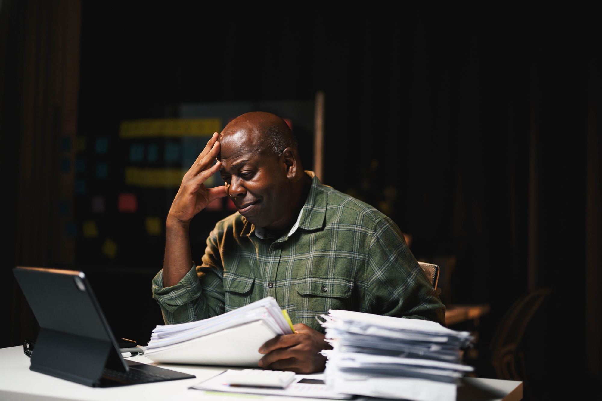 African American Man Working Late at Night in Office with Documents and Digital Tablet