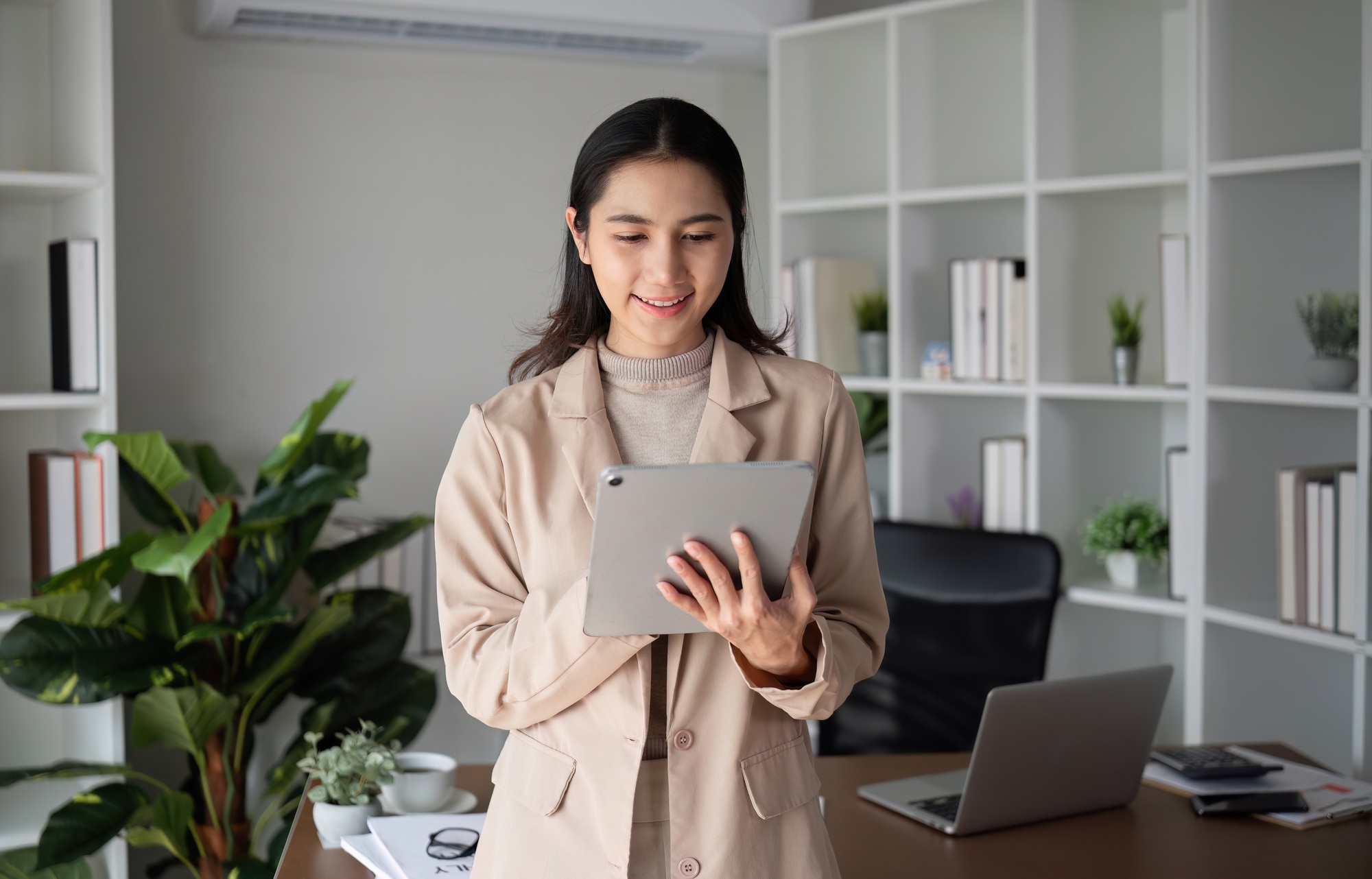 Asian businesswoman holding online business meeting via tablet in modern home office decorated with