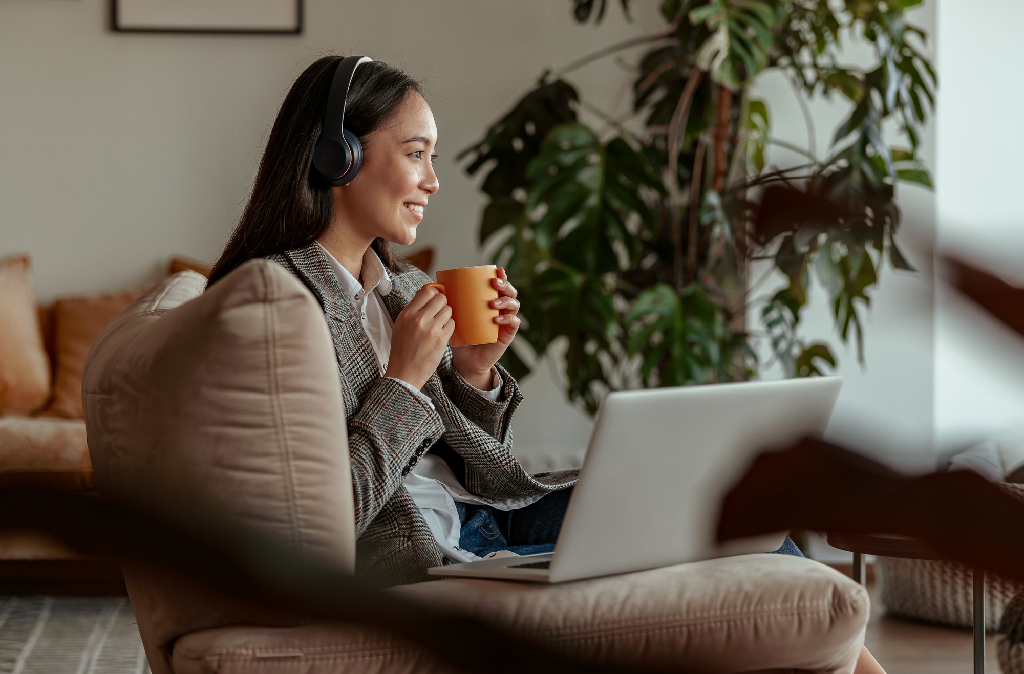 Attractive asian business woman listening music on headphones sitting at laptop with coffee
