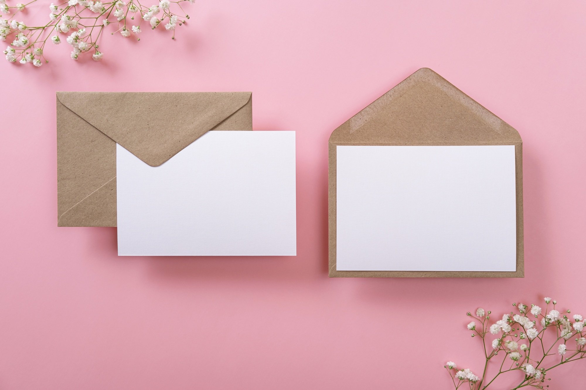 Blank greeting cards and envelopes with gypsophila on pink background.