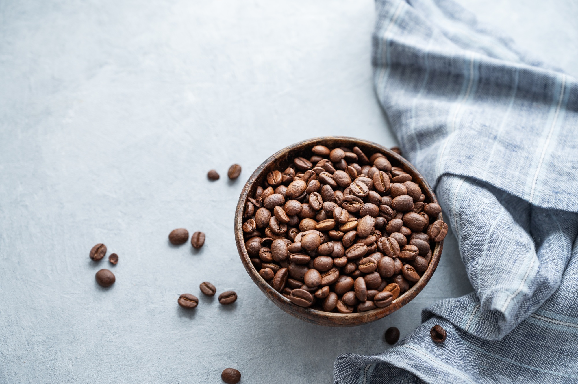 Bowl of roasted coffee beans on table with linen cloth in natural light setup.