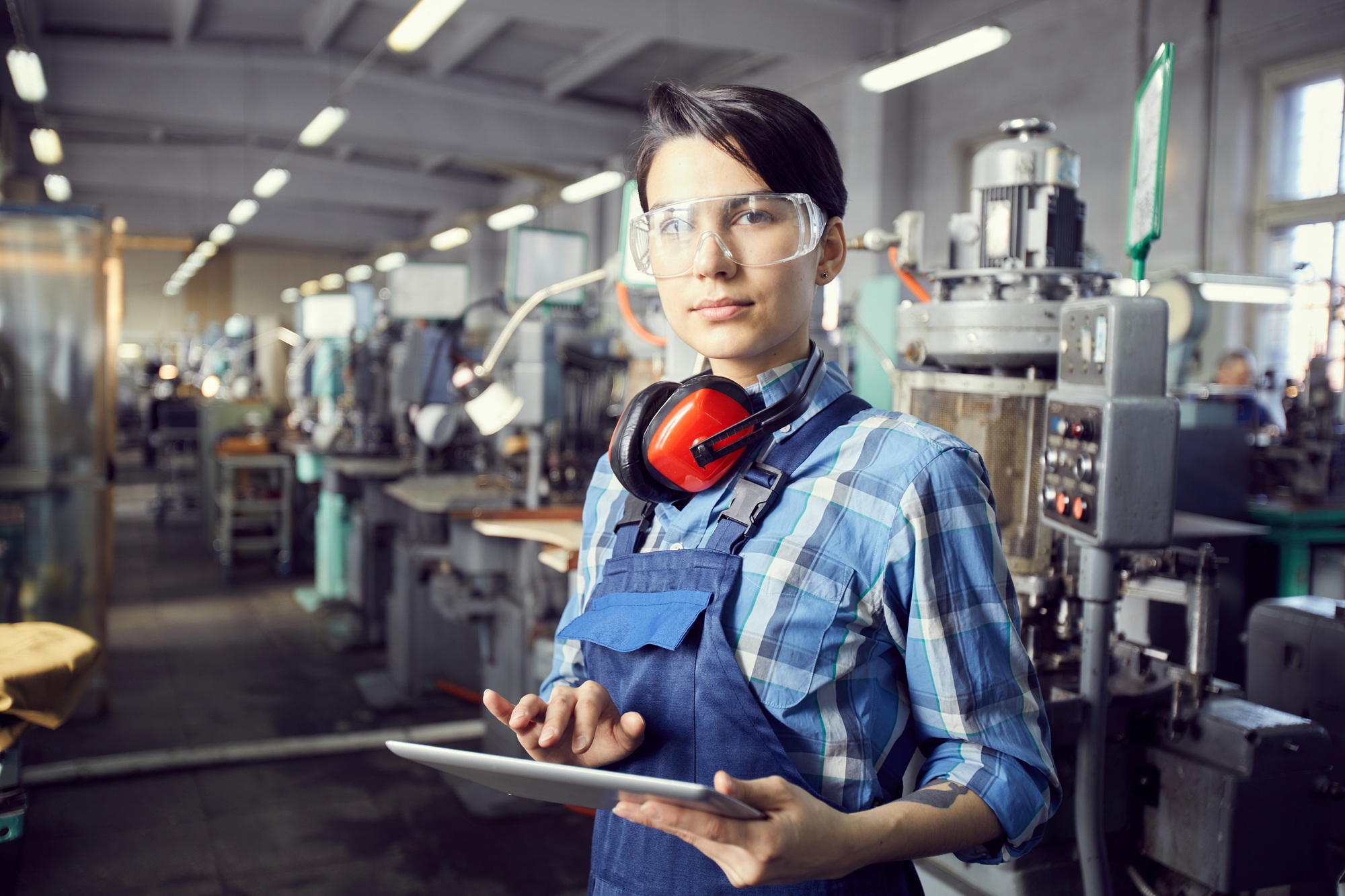 Brunette woman examining setups of factory machine via tablet app