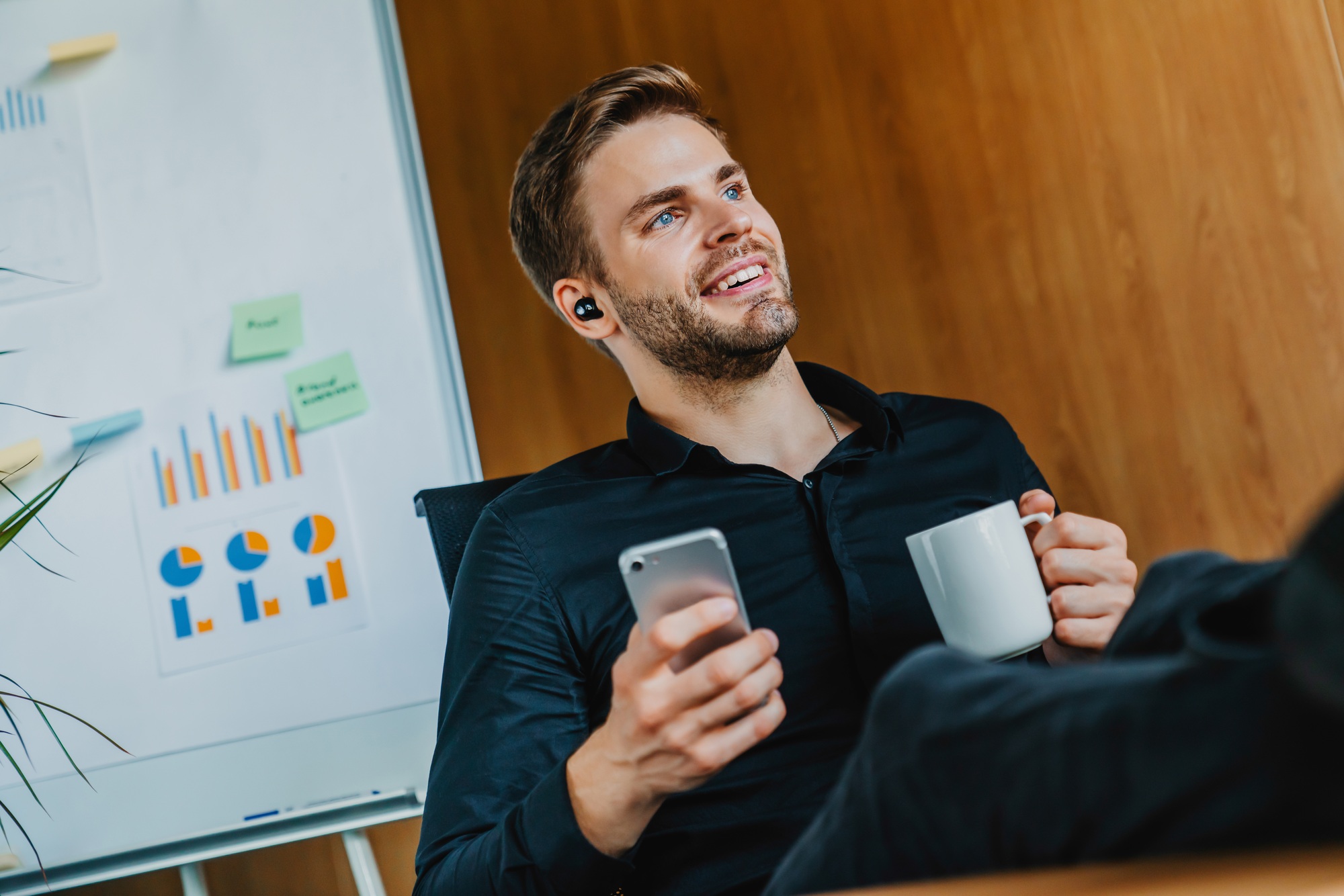 Business man listening music and holding cup with smartphone in modern office