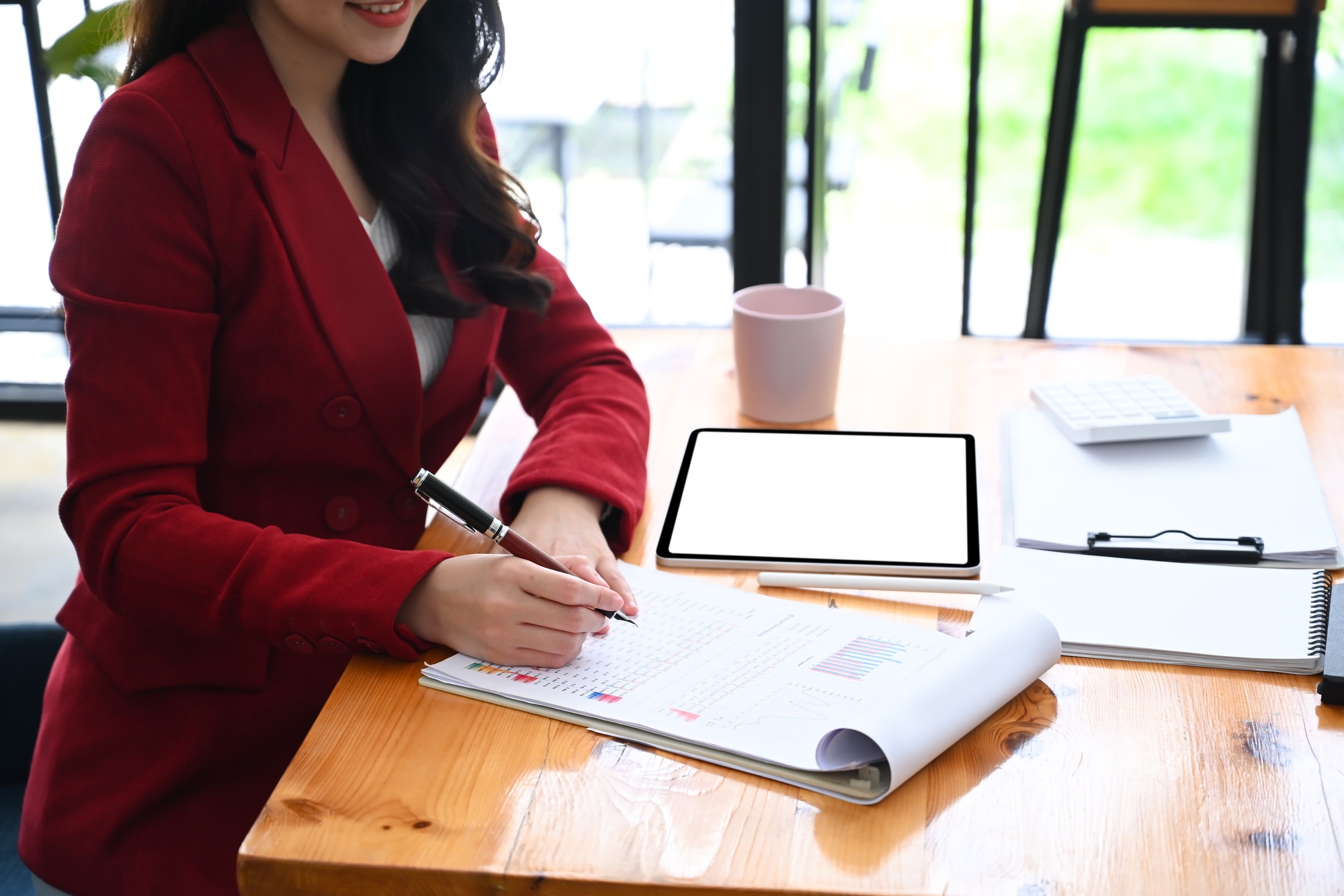 Businesswoman using digital tablet and writing information on document.