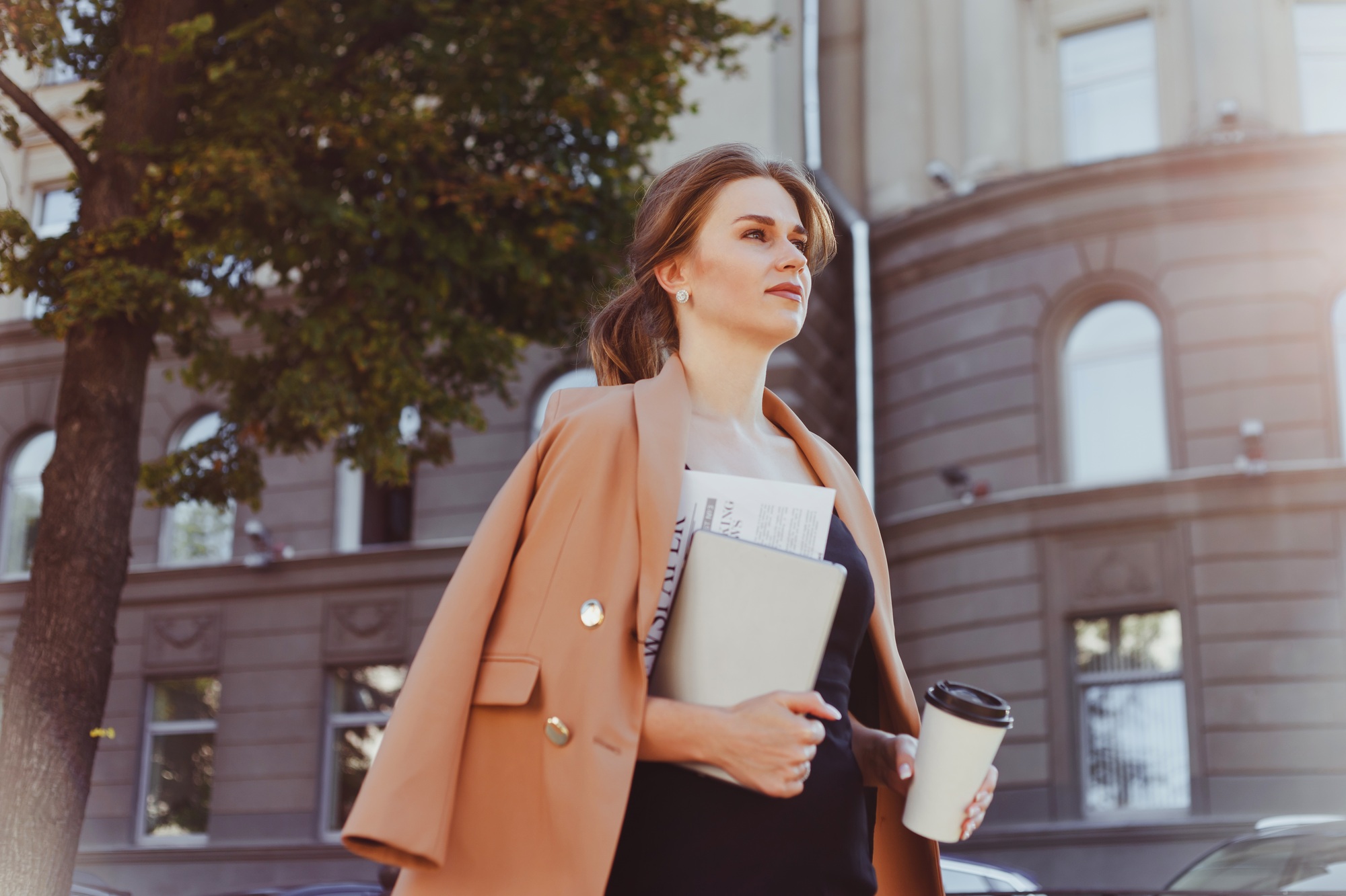 Businesswoman with coffee to go, digital tablet and documents walking street in morning