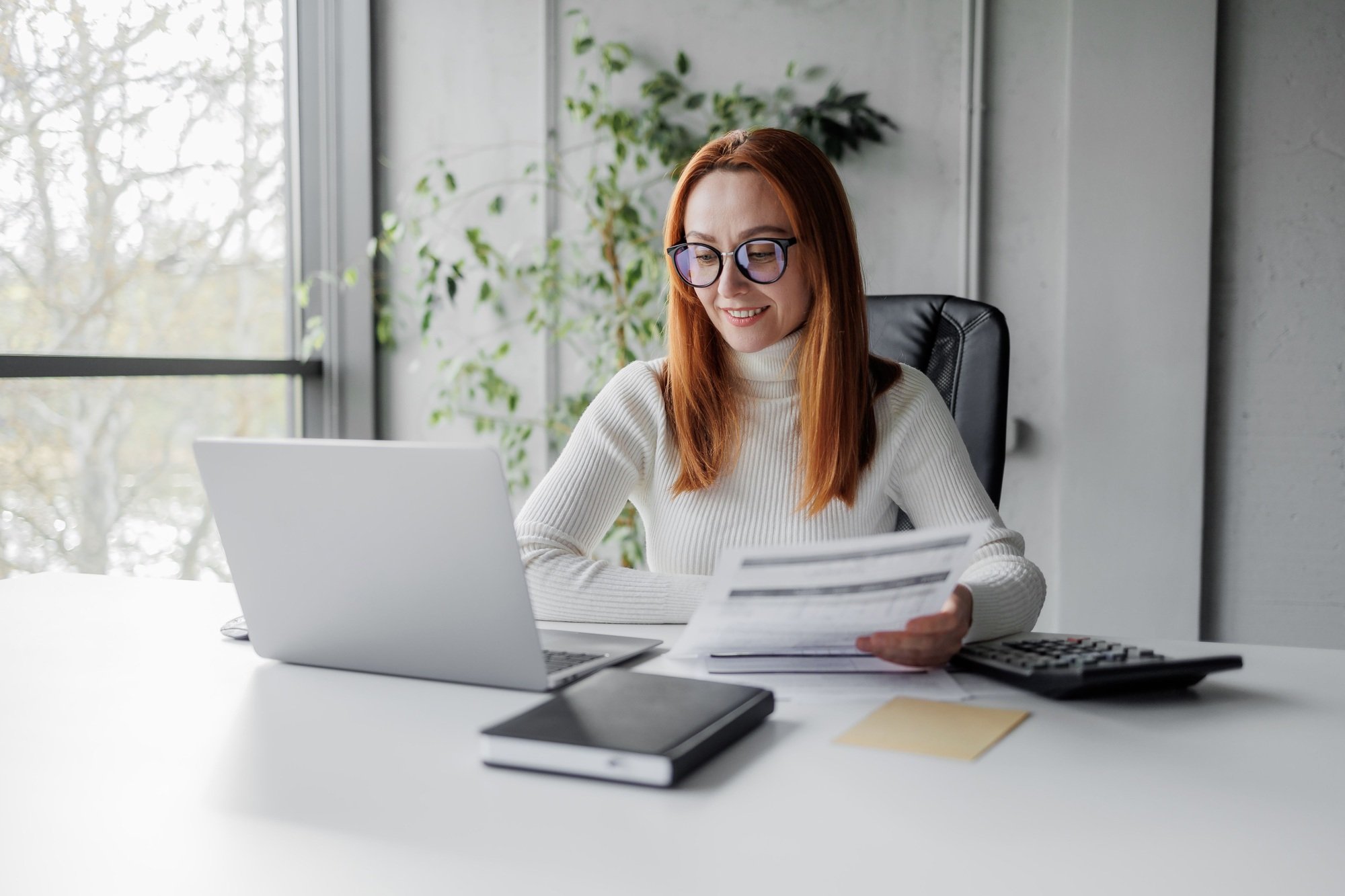 Businesswoman with invoices and documents calculating rates and KPIs in an office