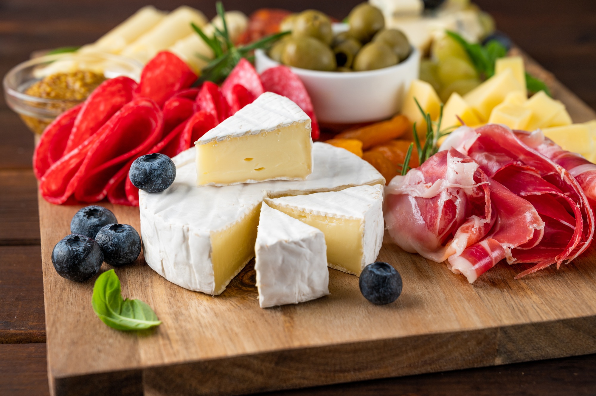 Charcuterie board with a variety of cheeses, salami, chorizzo, prosciutto, nuts, bread, berries