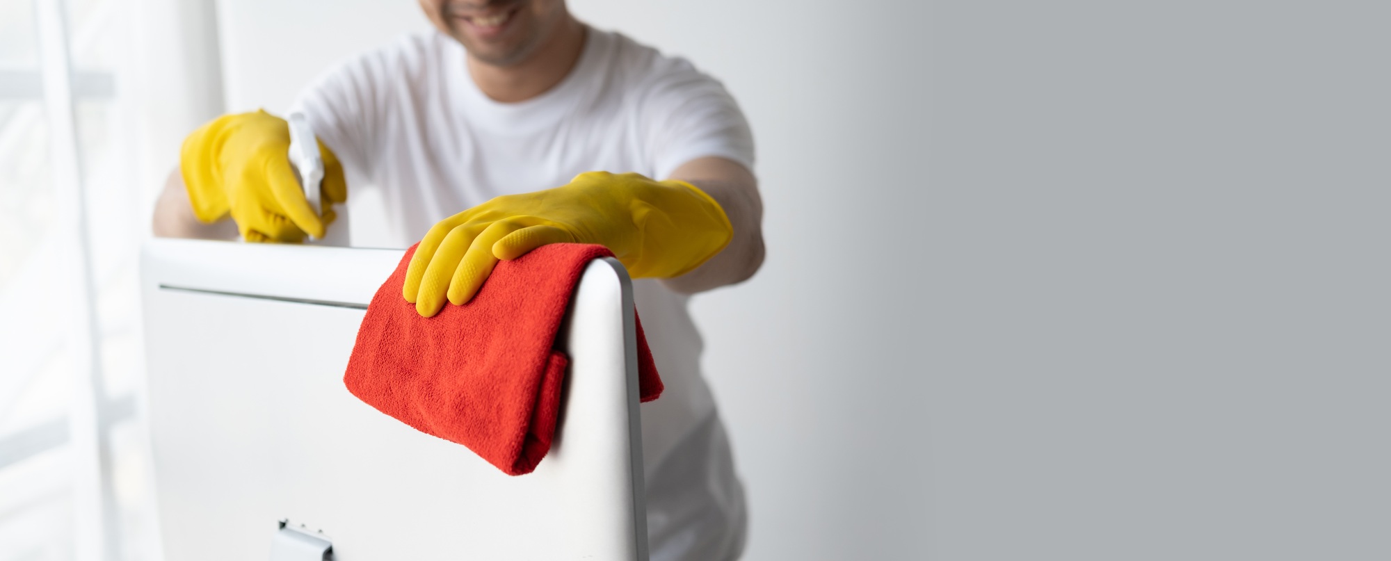 Close up view of man cleaning desktop computer using clothes. Cleaning office desk concept.