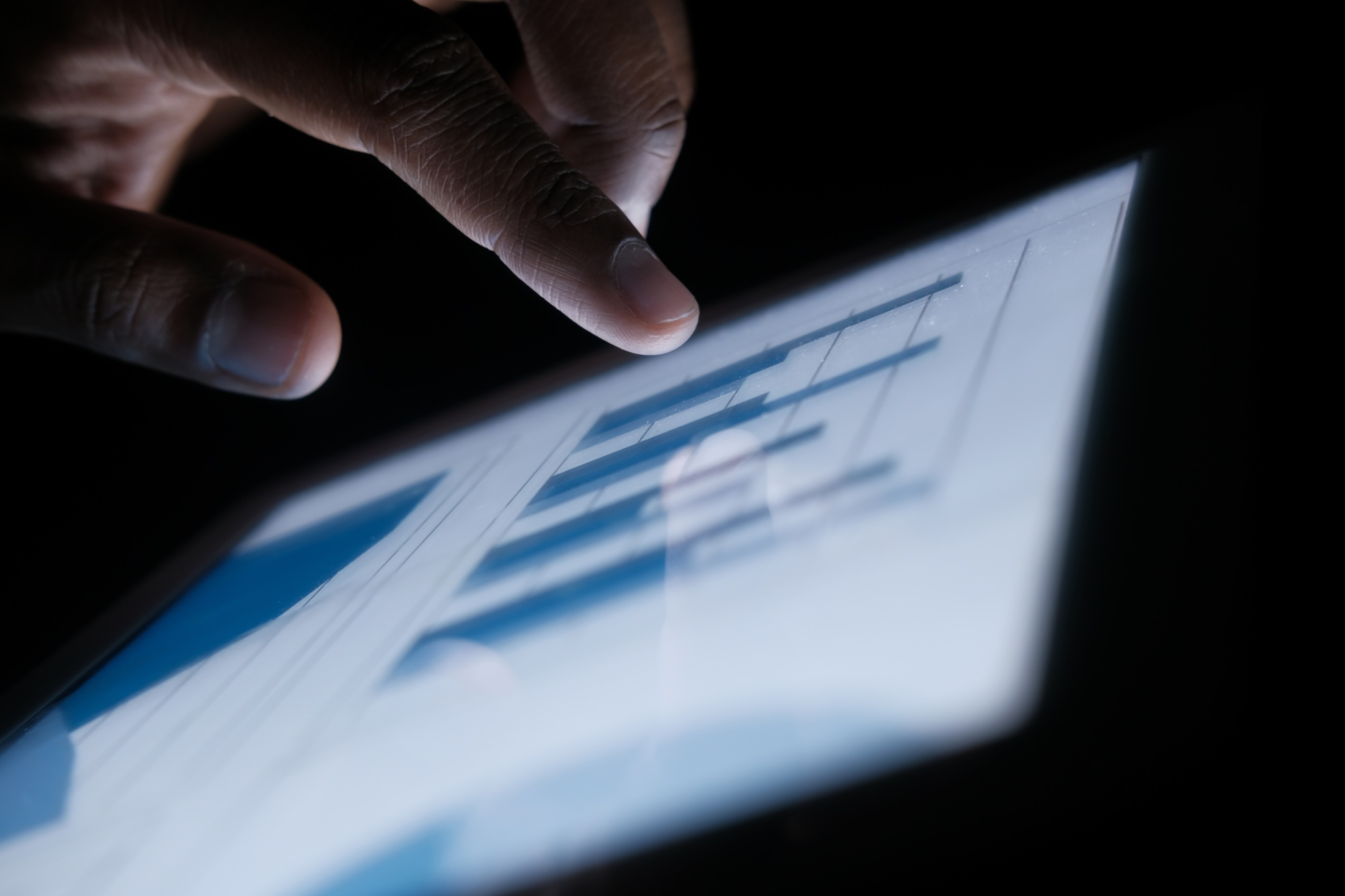 Closeup of a hand interacting with a digital tablet showing various data charts and info