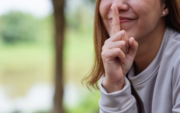 Closeup of a young asian woman with index finger on lips, asking to be quiet or keep secret