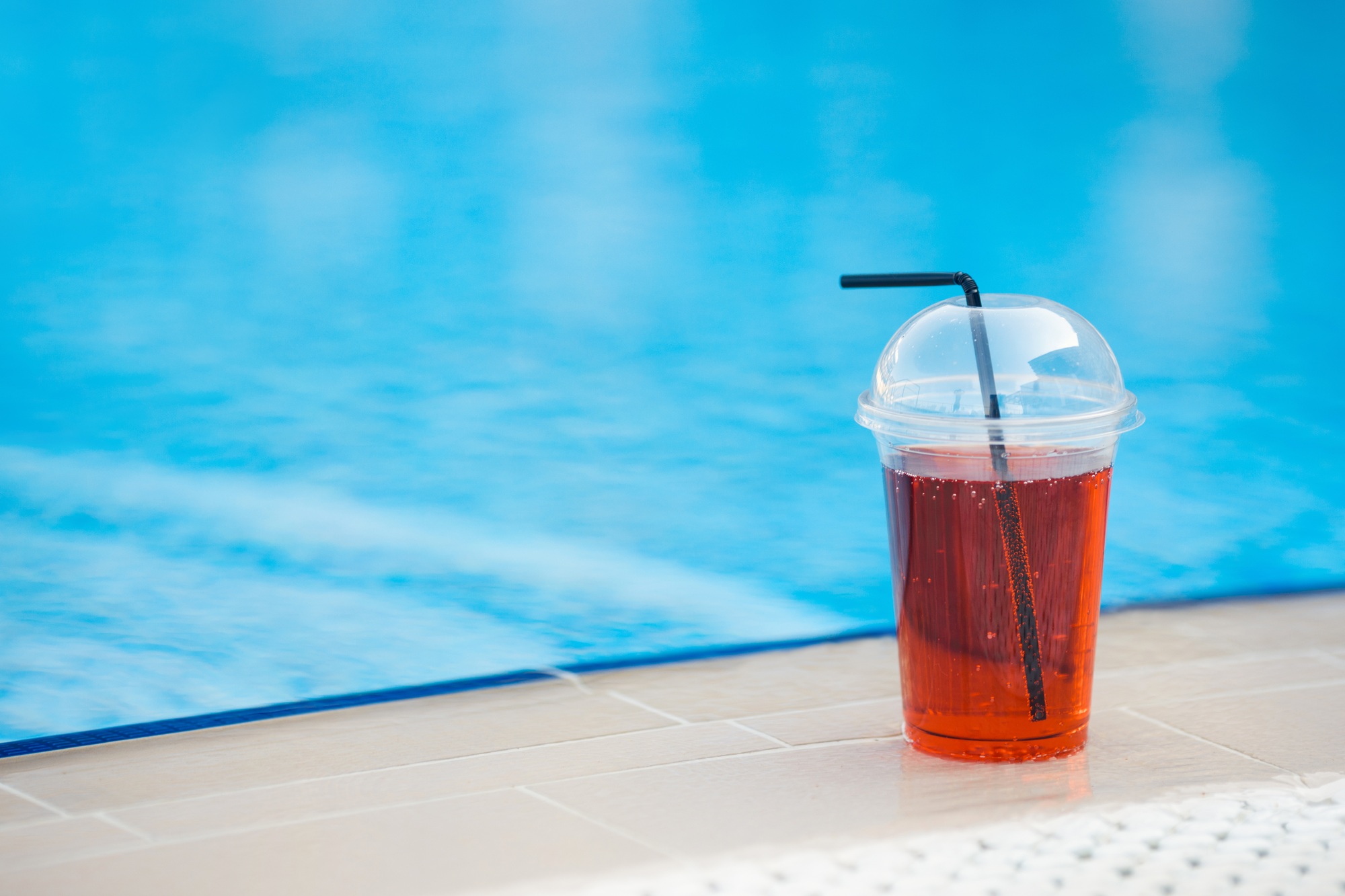 Cool drink juice to go in a plastic glass with a straw stands by the swimming pool bar at hotel