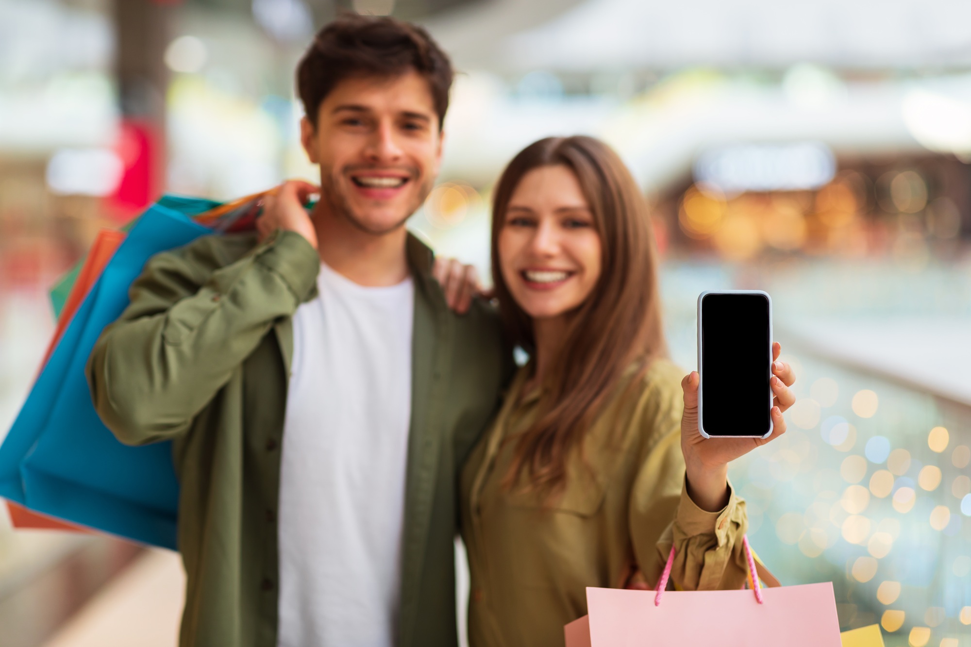 Couple Showing Phone Advertising Application For Mobile Shopping In Mall