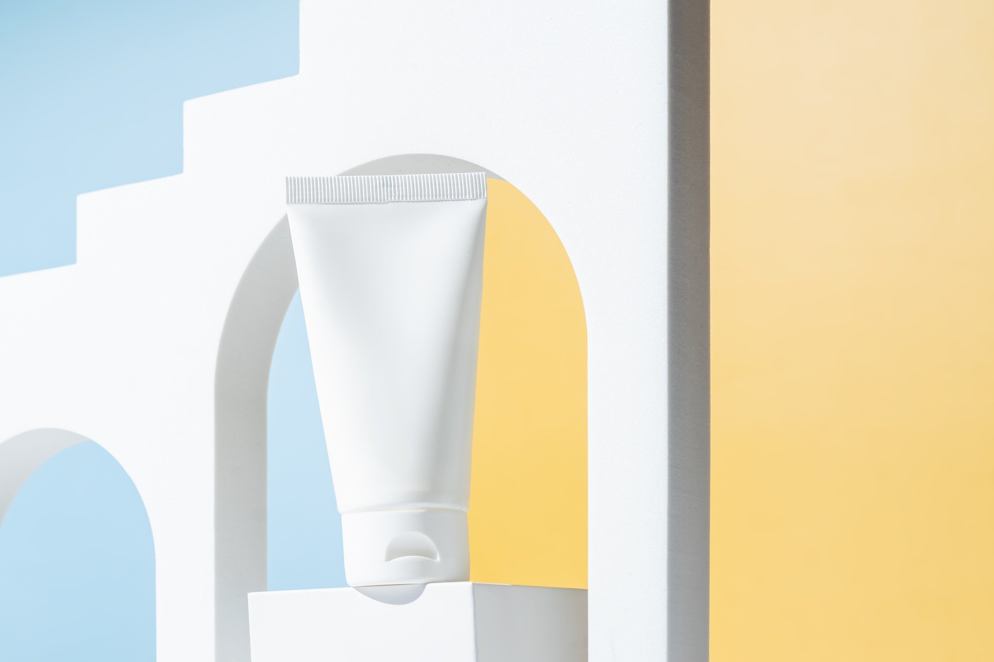 Cream tube with cream branding concept on cocncrete podium on blue and yellow background. Cosmetic