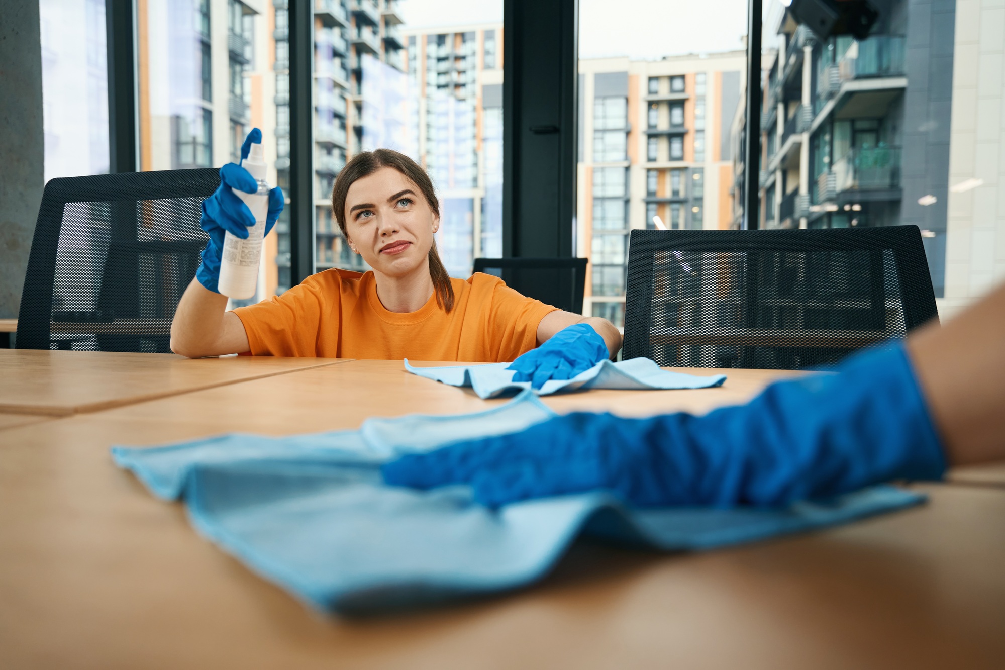 Cute cleaning company employees in rubber protective gloves disinfect desktops