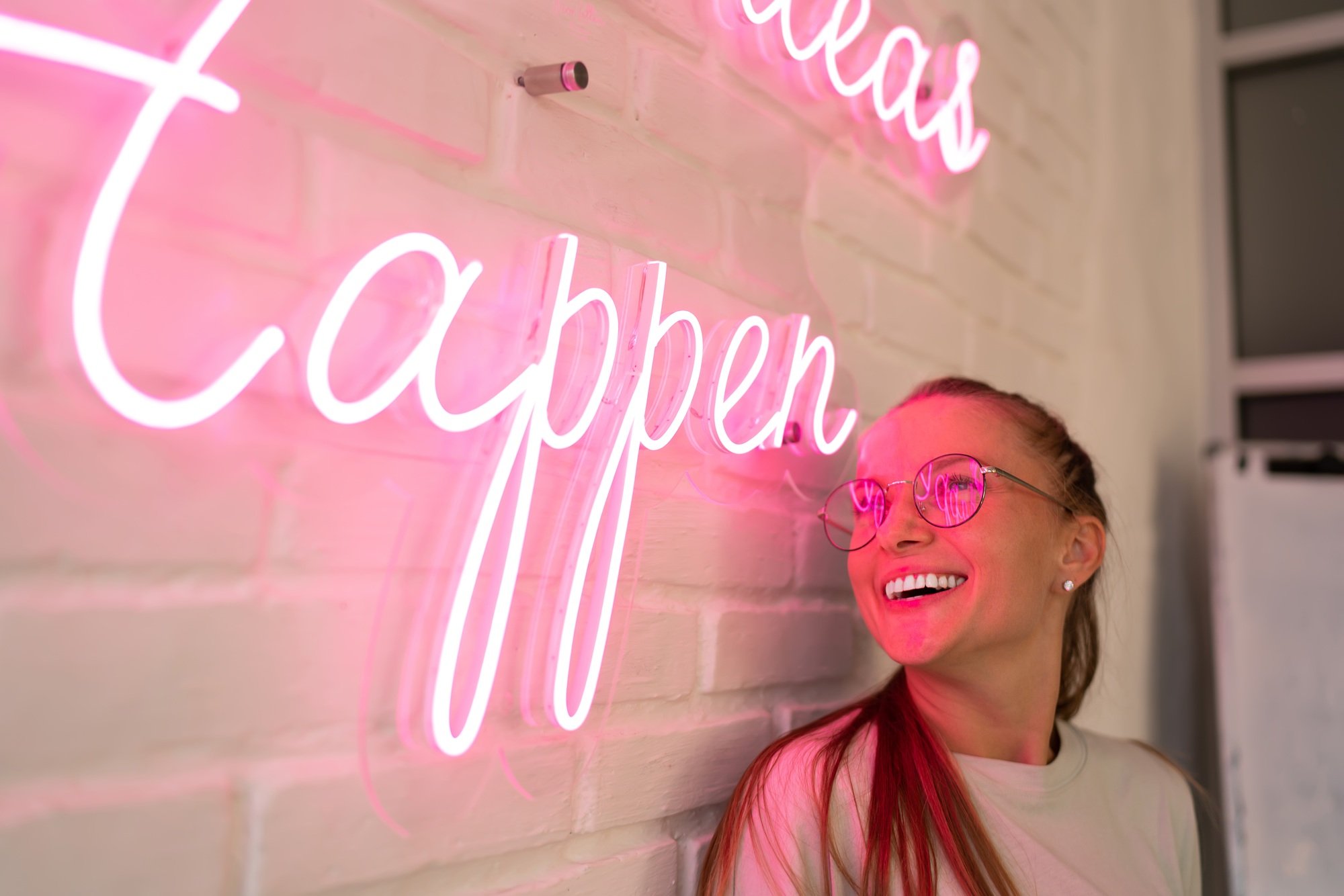 excited female millennial in spectacles reading colorful neon text and smiling