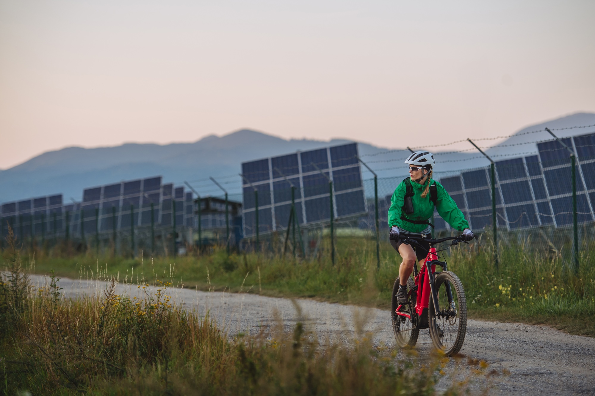 Female cyclist riding in front of solar panels at a solar farm.