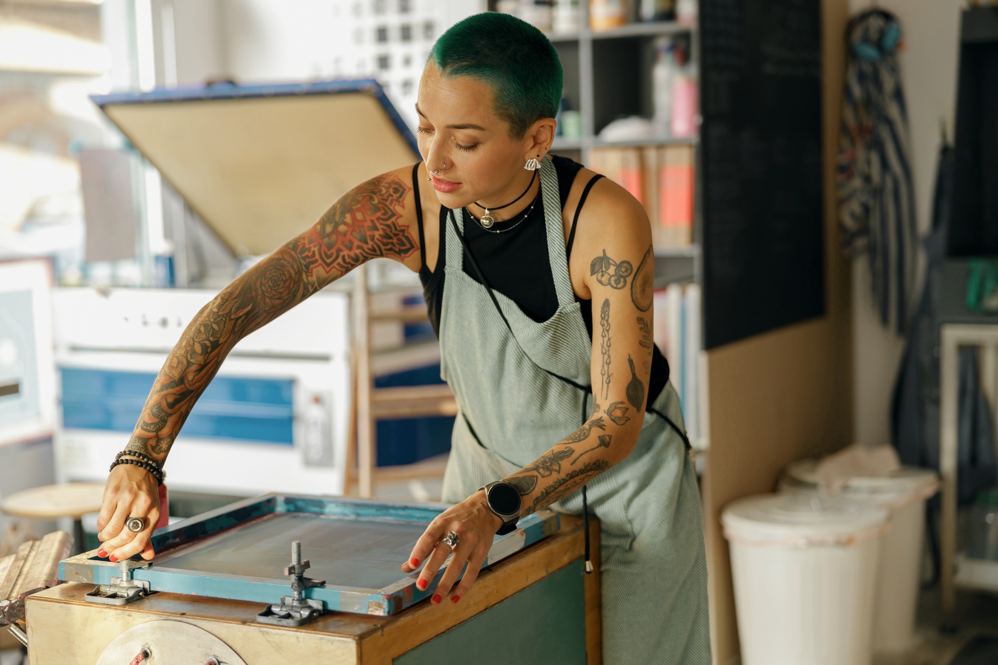 Female worker with squeegee is printing images on textile by silkscreen method in a design