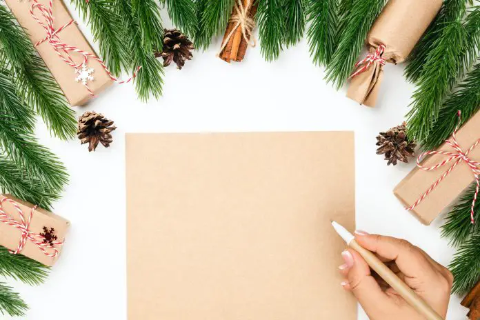 Flat lay, mock-up wish list and female hand writing checklist on table with decorations of fir