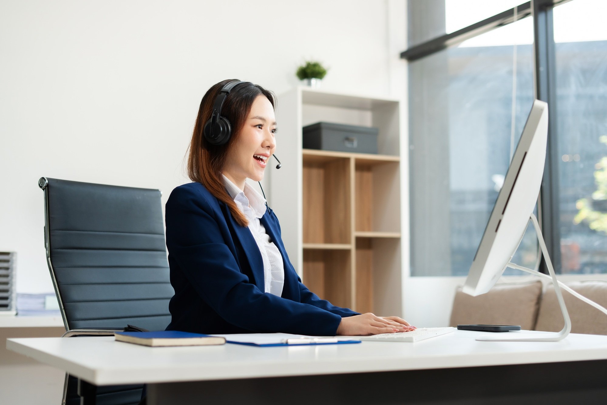 Friendly smiling female call-center agent with headset working on support hotline in office.