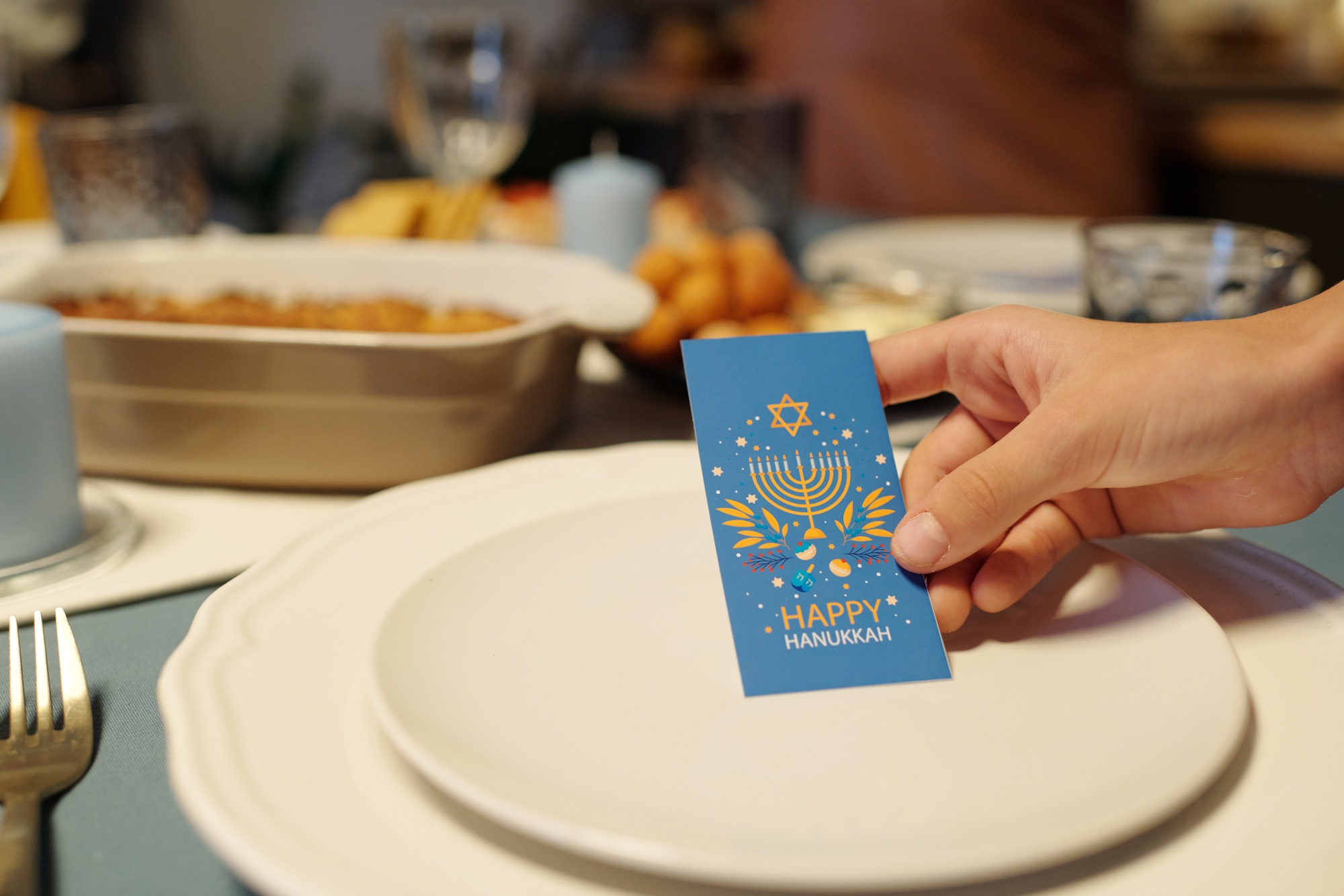 Hand of girl holding blue Hanukkah greeting card over plate