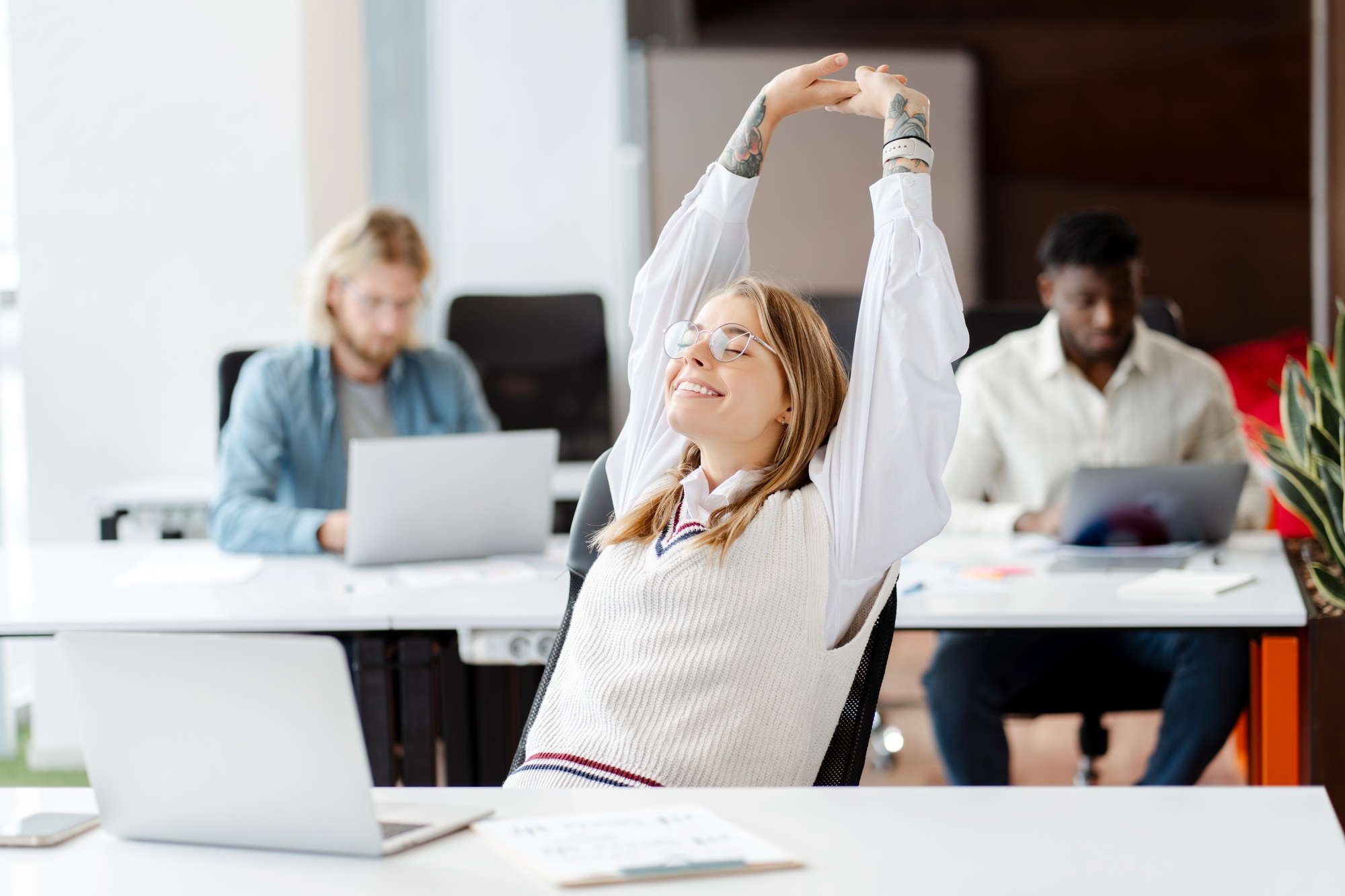 Happy businesswoman stretching at workplace with laptop on desk