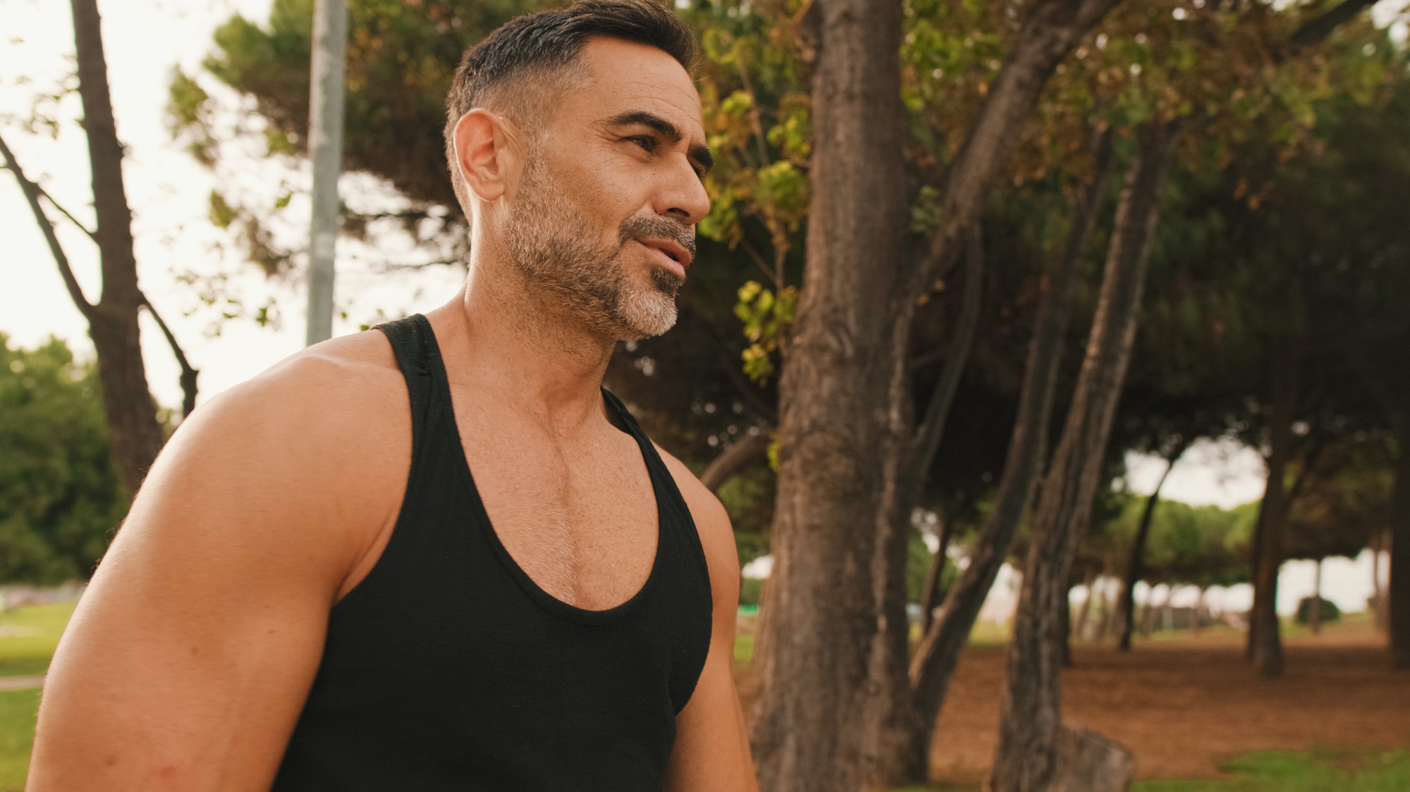 Happy mature muscular man in sportswear walking in the park after training, looking around