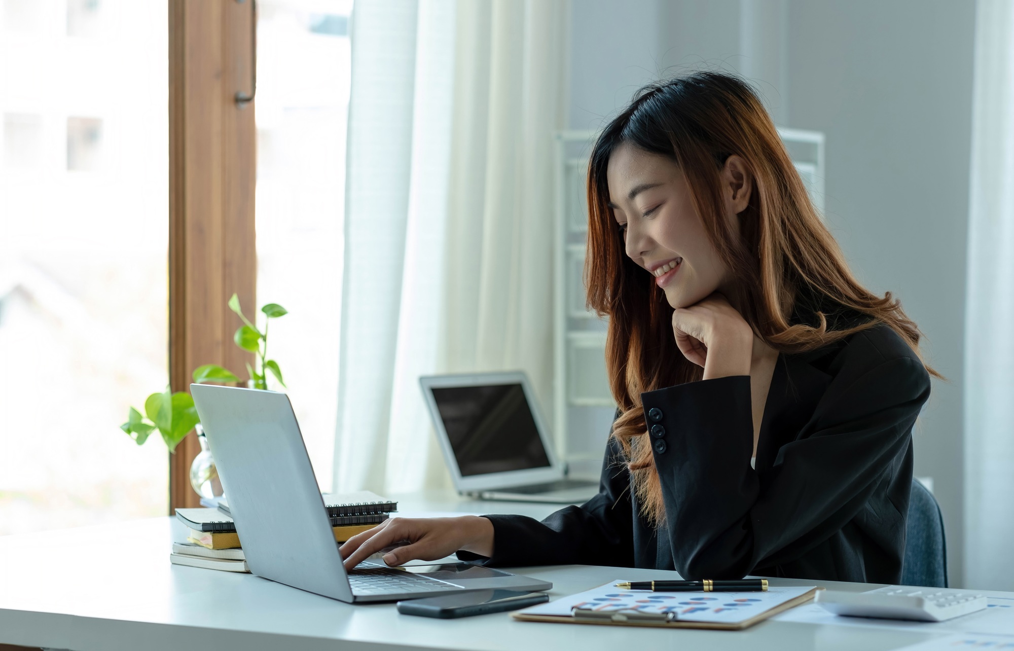 Happy young asian businesswoman sitting on her workplace in the office. Young woman working at
