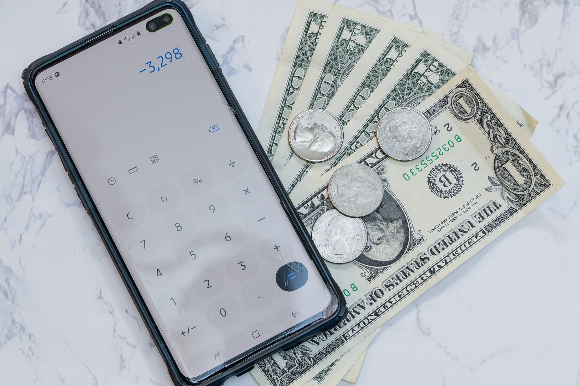 High angle view of a phone with the calculator app on it on dollars and coins on the table