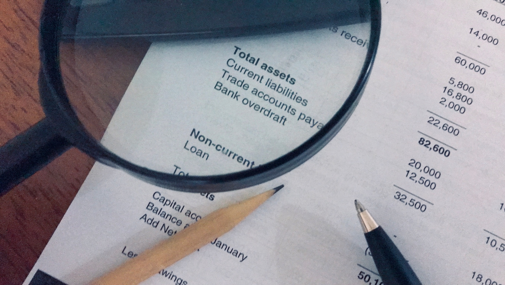 Income statement, balance sheet, pen, pencil, calculator and magnifying glass on wooden background