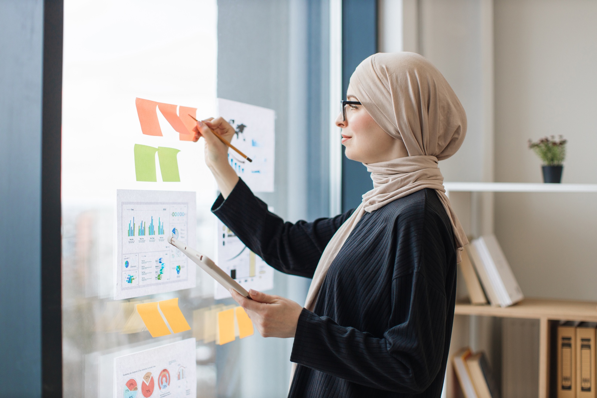 Lady with tablet writing notes on stickers near infographics
