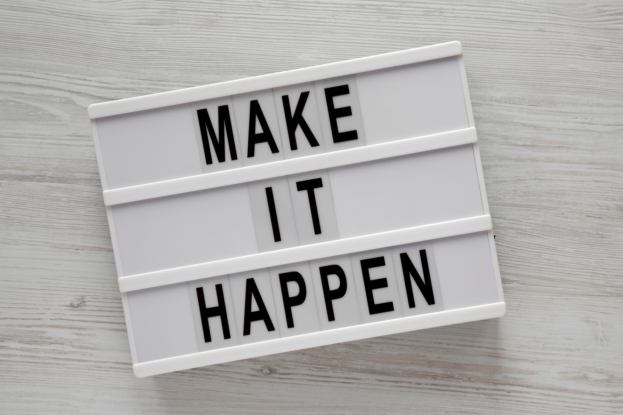 Lightbox with words 'Make it happen' on a white wooden background, top view.