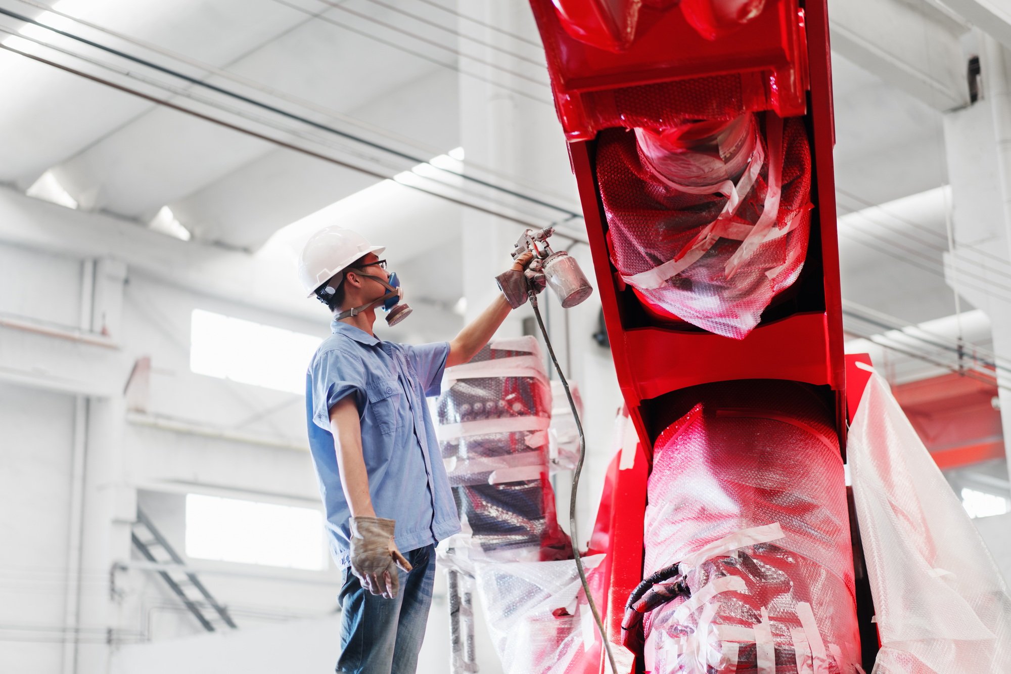 Male factory worker spray painting a red crane in factory, China