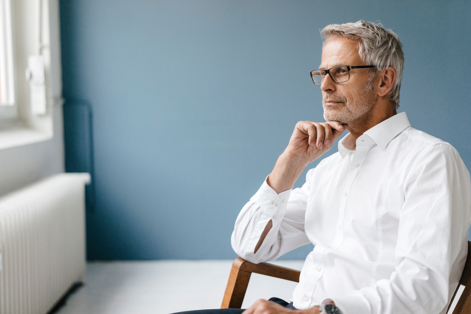 Manager sitting in chair in his office, looking out of the window, thinking