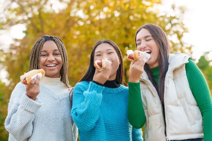 Multiethnic friends joking while eating hot dog in a park